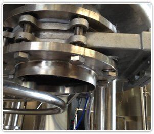 Close-up of a stainless steel pipe flange connection secured with bolts on industrial manufacturing equipment.