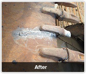 A close-up of heavy machinery bucket teeth repaired with weld beads on a rusted metal surface, labeled 