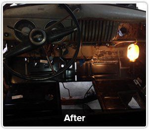 The interior of a classic car dashboard showing a freshly installed black metal floor panel, illuminated by a work light.