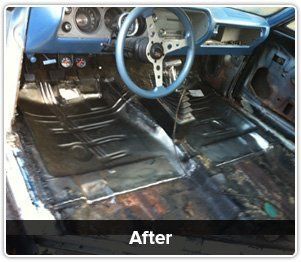 Interior of a classic car showing newly installed black metal floor pans under the dashboard and steering wheel.