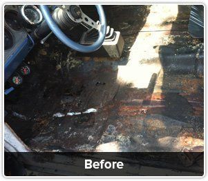 A rusted, stripped car floor interior with a steering wheel and gauges, labeled 