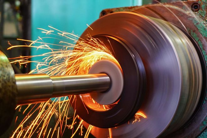 A metalworking machine grinds a cylindrical part, creating a bright spray of sparks.