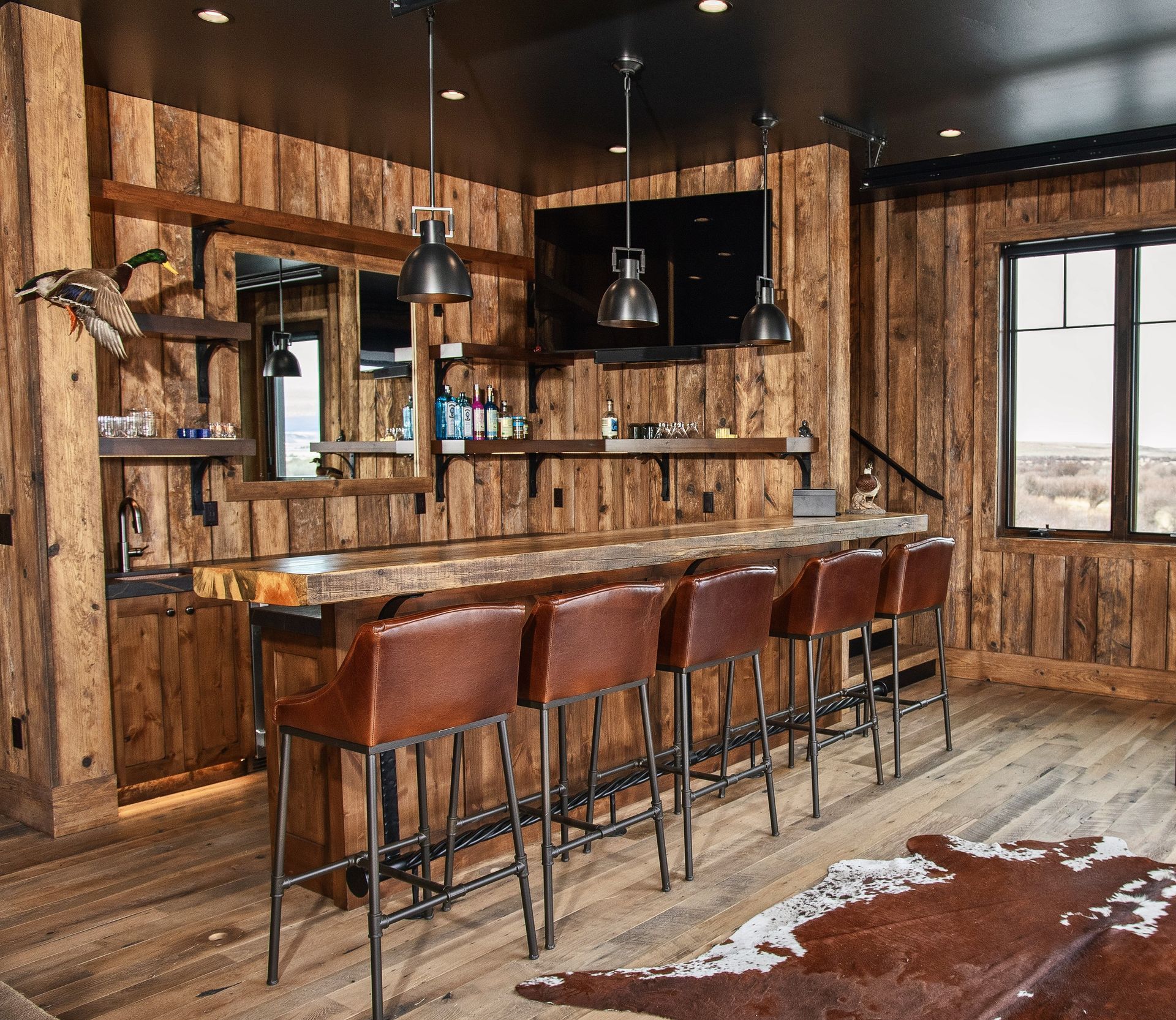 Rustic home bar with wood paneling, leather barstools, and a cowhide rug.