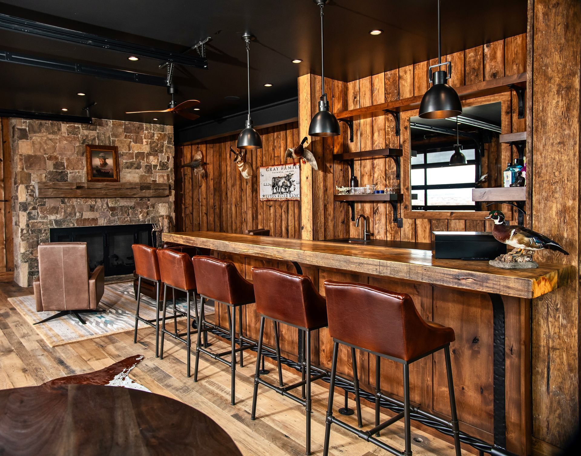 Rustic bar with wood paneling, stone fireplace, leather bar stools, and pendant lights.