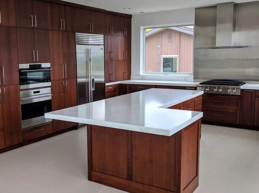 Modern kitchen with cherry wood cabinets, white countertops, stainless steel appliances.
