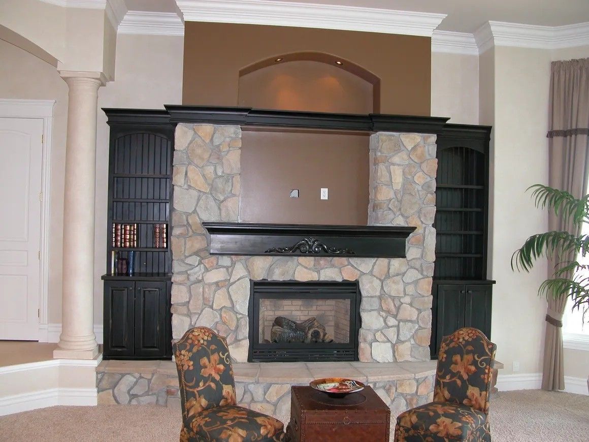 Stone fireplace with black cabinets and a brown wall, flanked by patterned chairs.