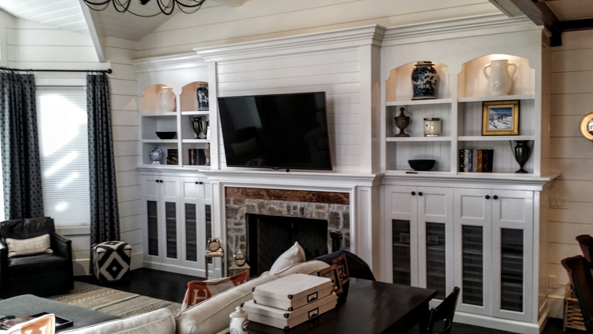 Living room with white built-in shelving around a fireplace and a large TV, dark furniture, and decor.