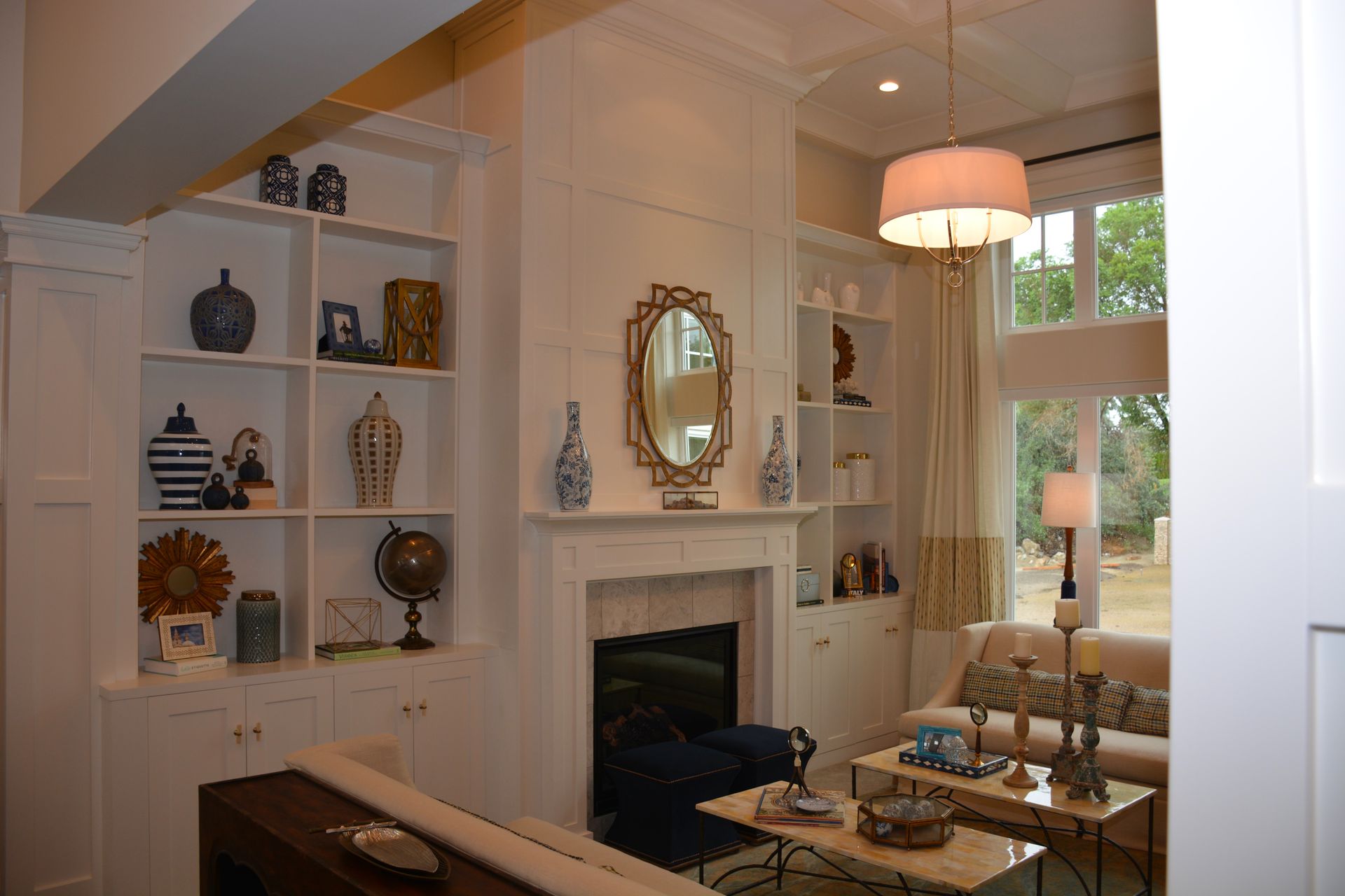 Living room with white built-in bookshelves, fireplace, sofa, and coffee tables; decorated with blue and gold accents.