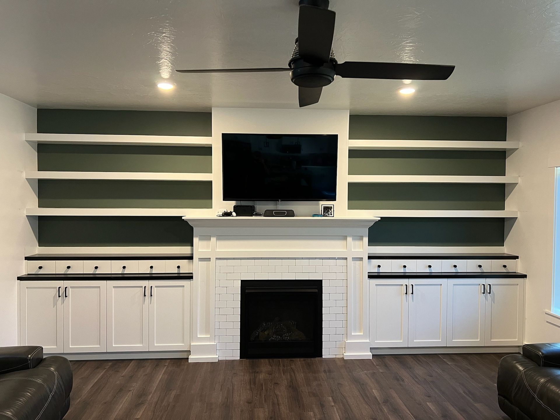 Living room with fireplace, TV, built-in shelves, cabinets, and black ceiling fan. White, green, and black color scheme.