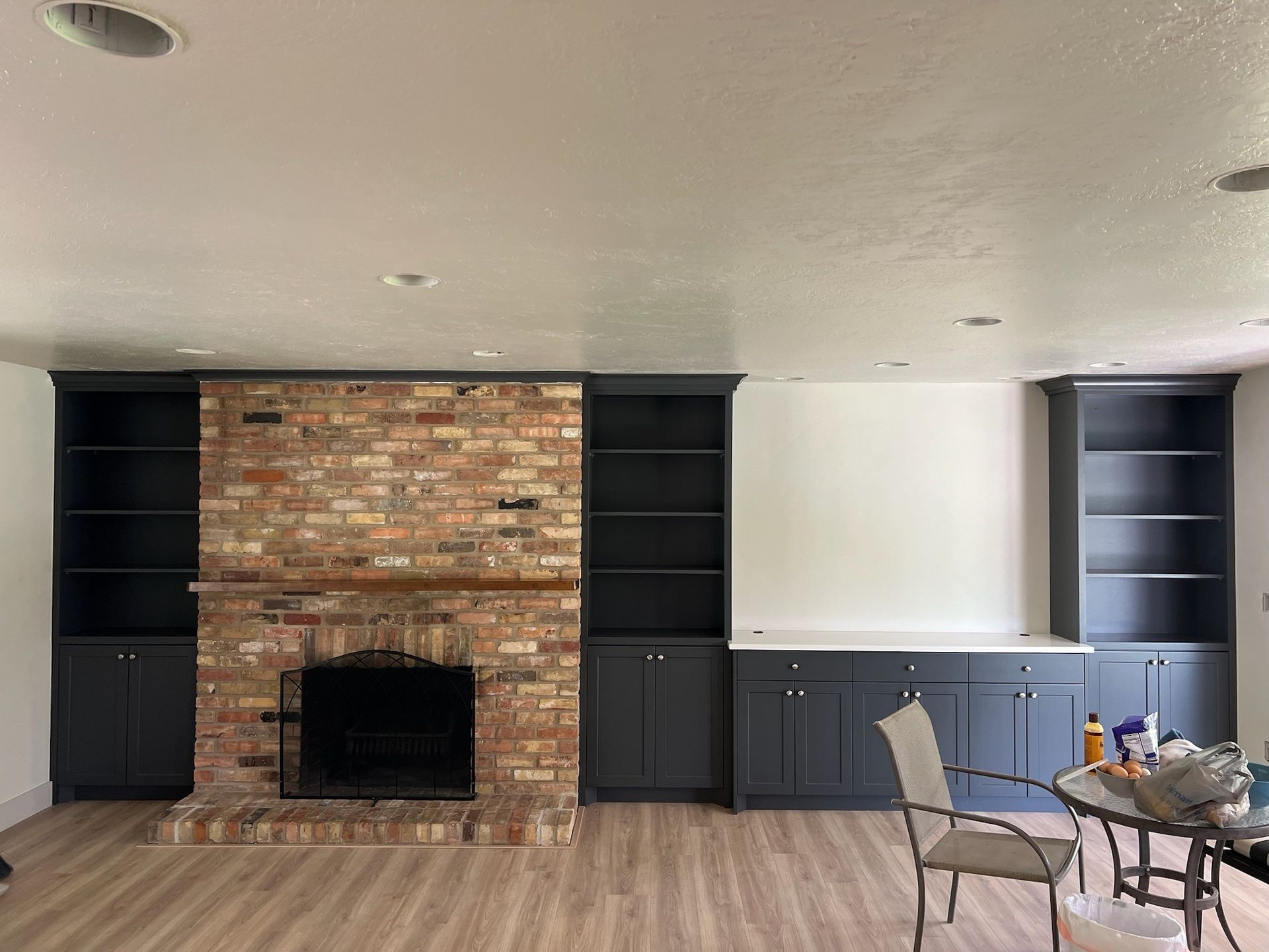 A room with a brick fireplace, built-in dark cabinets, and shelves; neutral walls and floor.