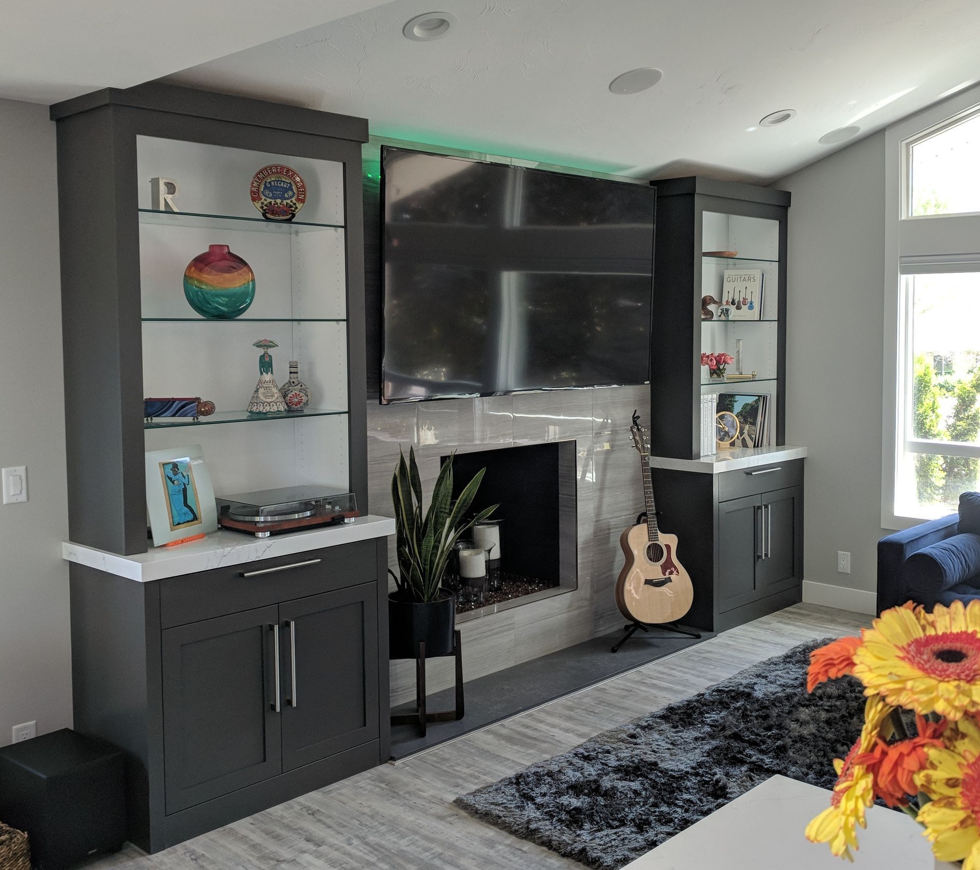 Living room with gray cabinets flanking a fireplace and TV. Guitar leans against the mantel.