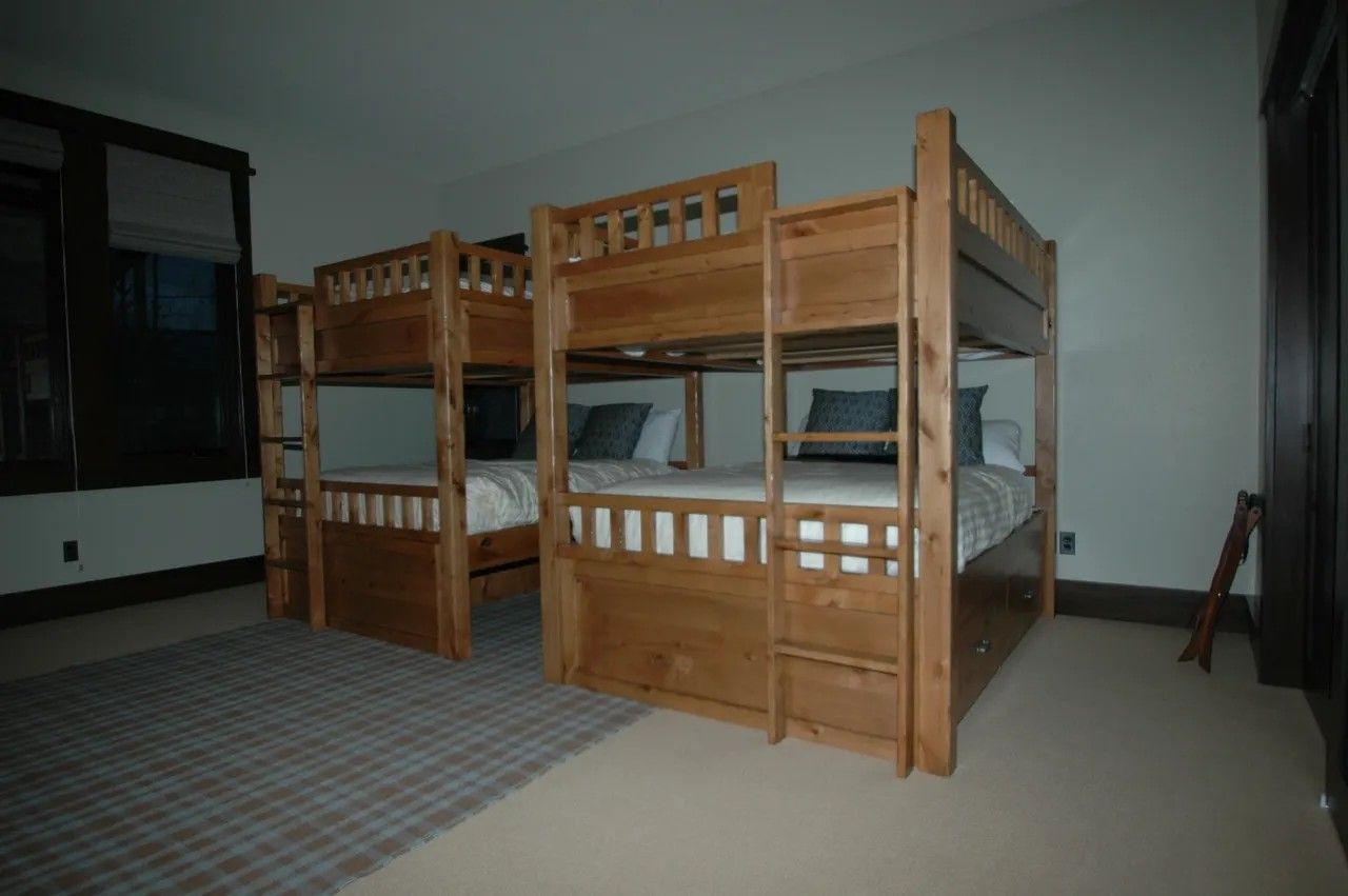 Two wooden bunk beds in a bedroom with a rug, window, and stool.