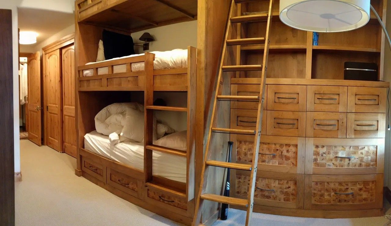 Wooden bunk beds with a ladder and built-in storage in a wood-paneled room.