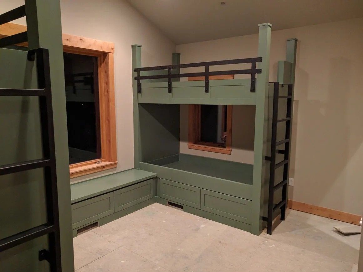 Green bunk bed with built-in bench and storage, near a window, in a room with tan walls.