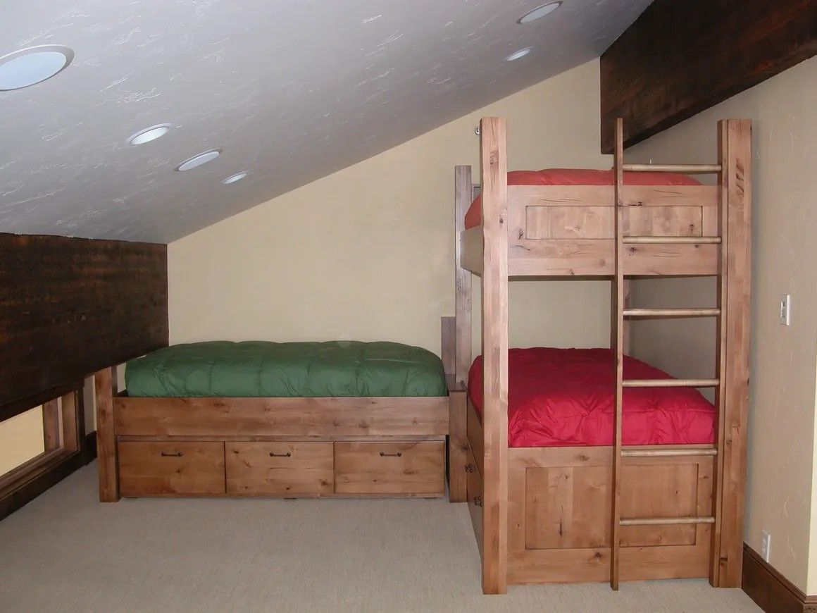 Bunk beds and a full-size bed in a small room with angled ceiling. Green and red bedding.