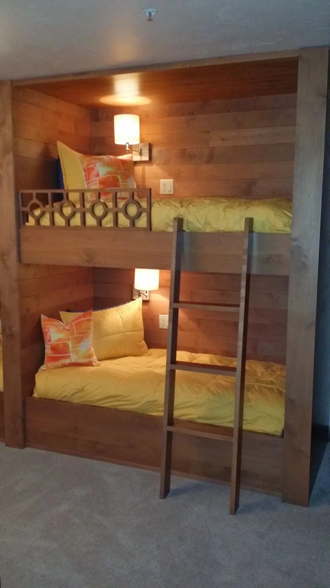 Wooden bunk beds with yellow bedding, pillows, and a ladder; built into a wall.