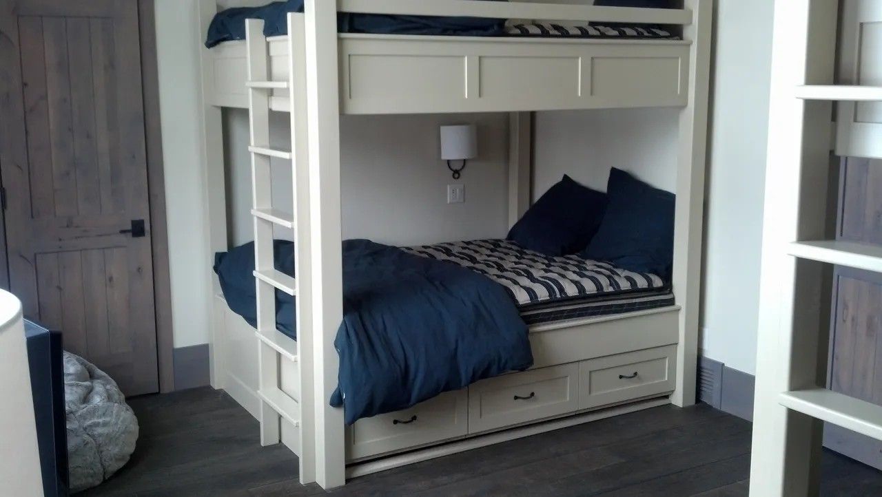 Cream-colored bunk beds in a recessed nook, with navy bedding, drawers, and a ladder.