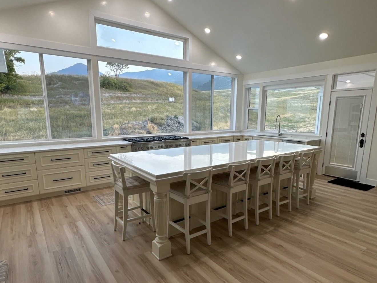 Spacious kitchen with a large island, light-colored cabinets and flooring, and mountain views through large windows.