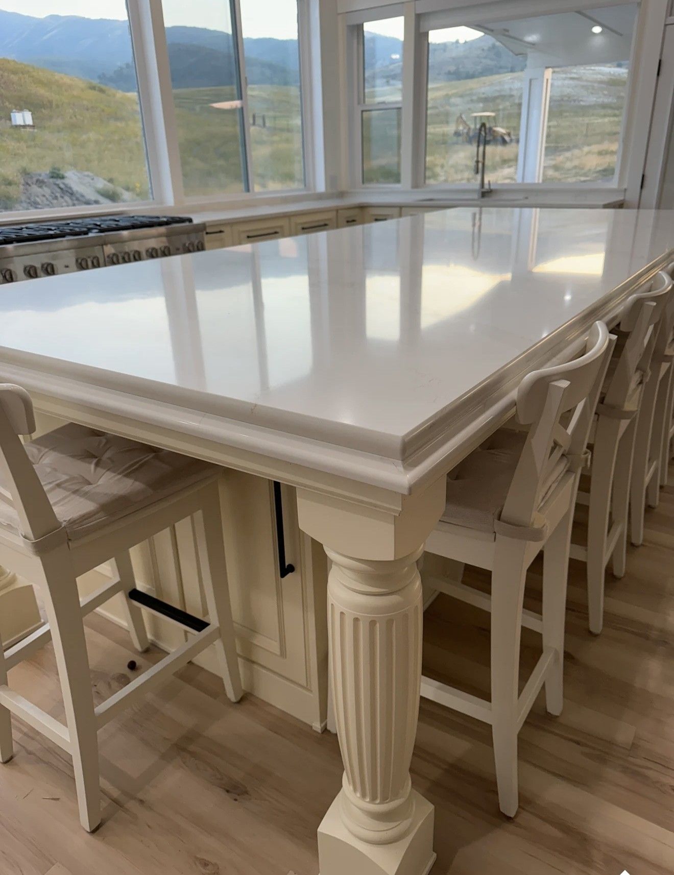 White kitchen island with seating, large windows, and a stainless steel range.