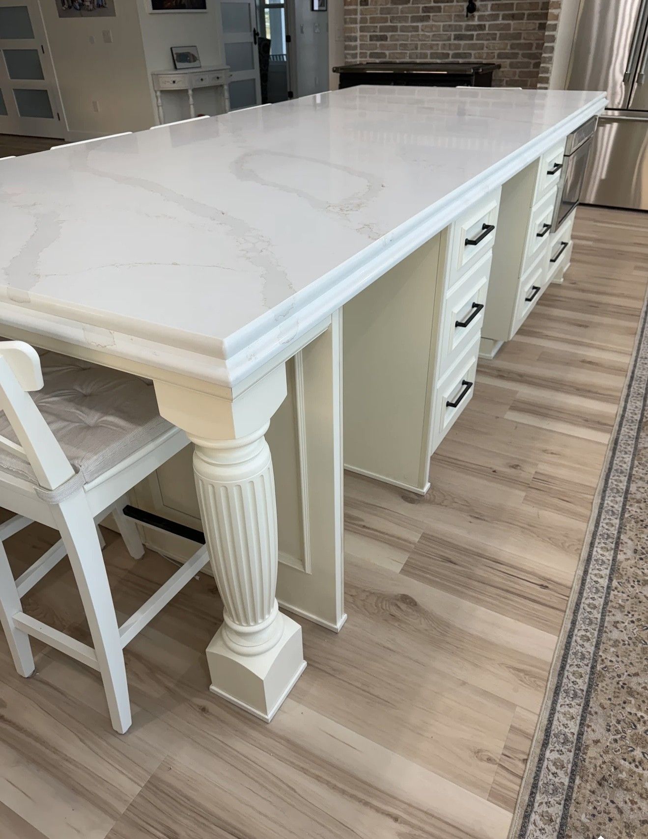 White kitchen island with marble countertop and drawers, column leg, wooden floor.