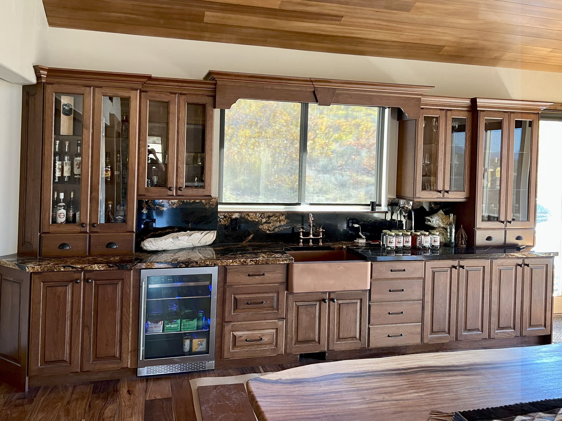 Wooden kitchen cabinets with a dark countertop, window, and a cooler.