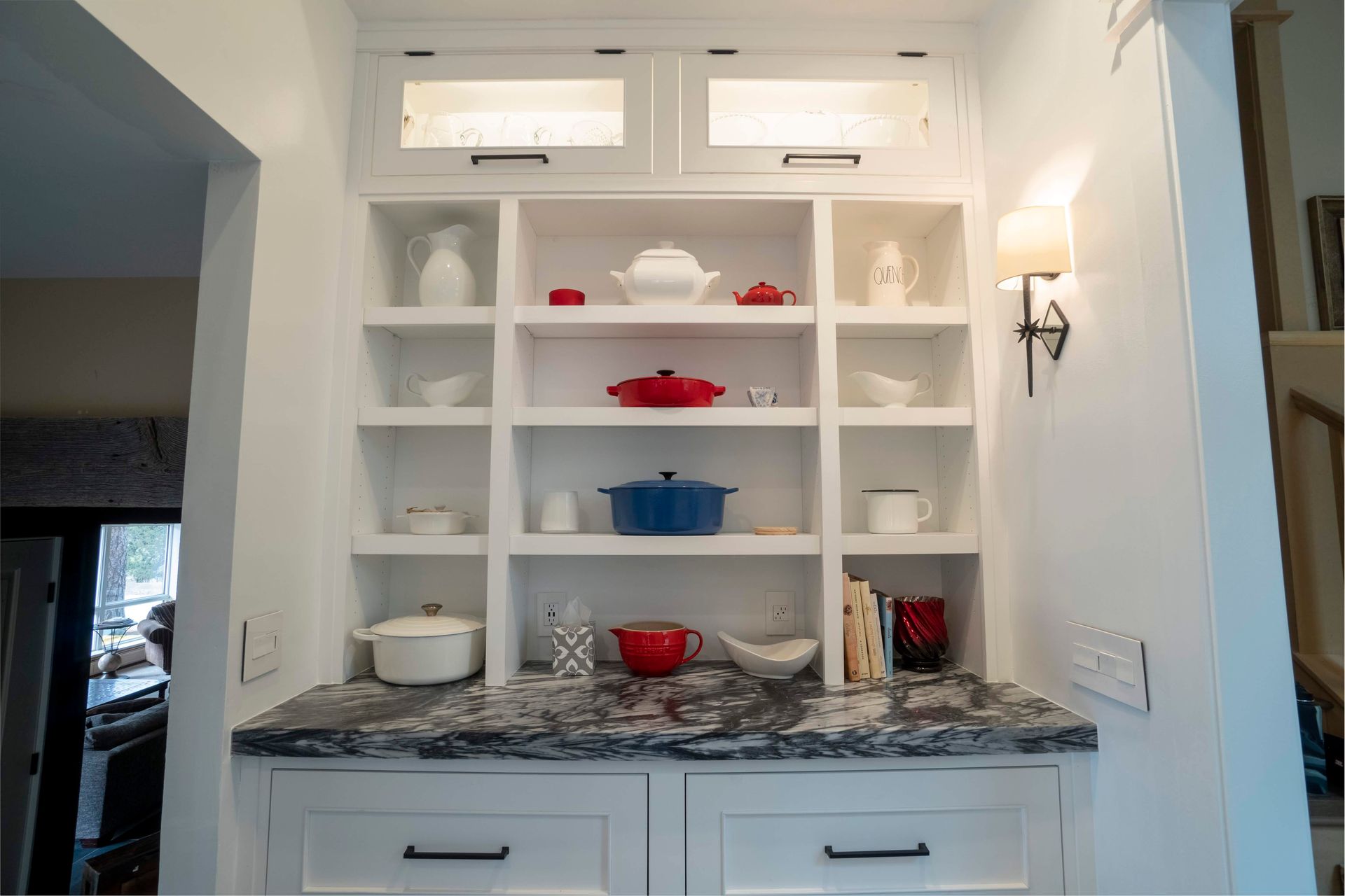 White built-in kitchen shelves with various dishes and cookware on a granite countertop.