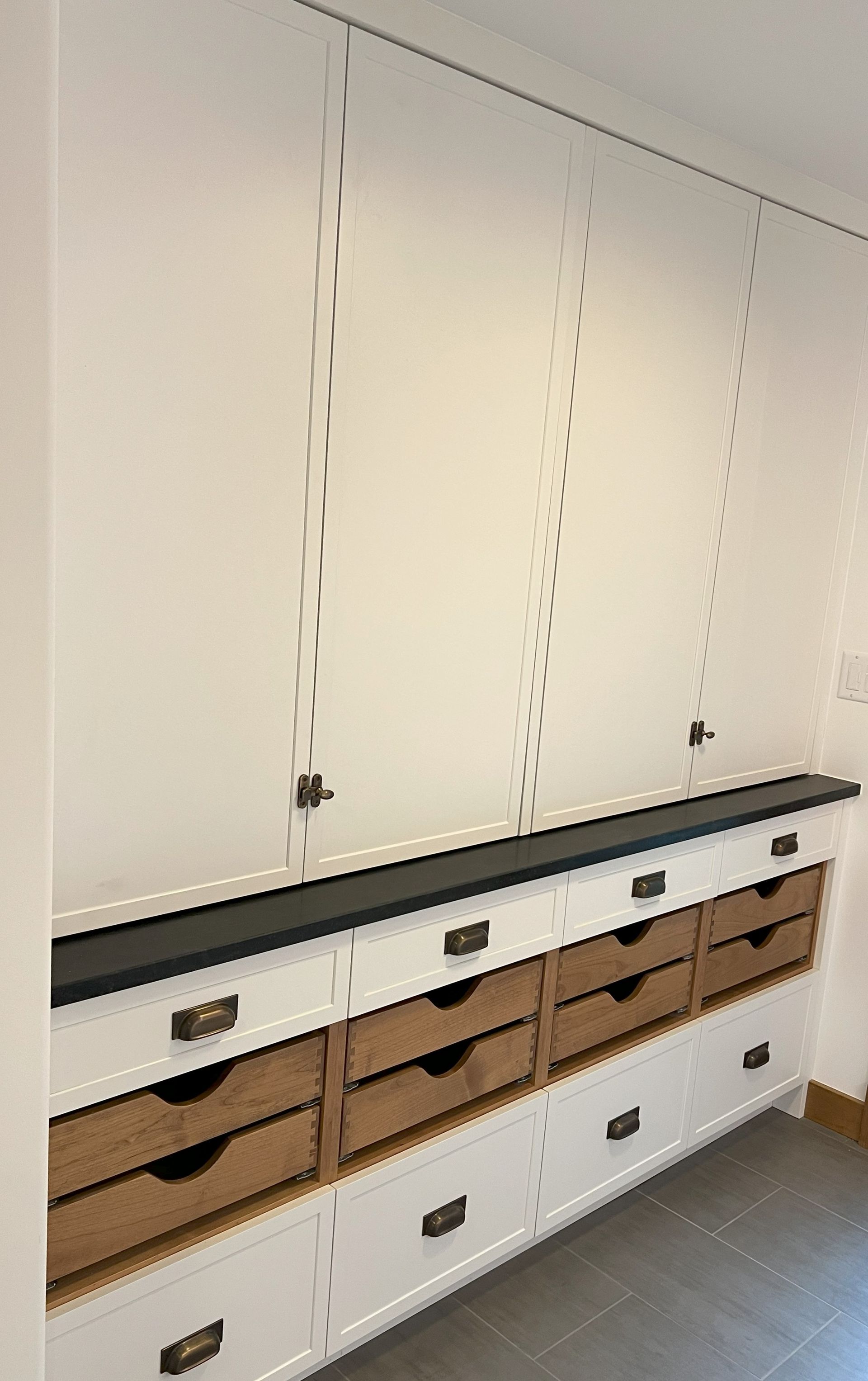 White wall cabinet with drawers, black countertop, and wooden drawer faces.