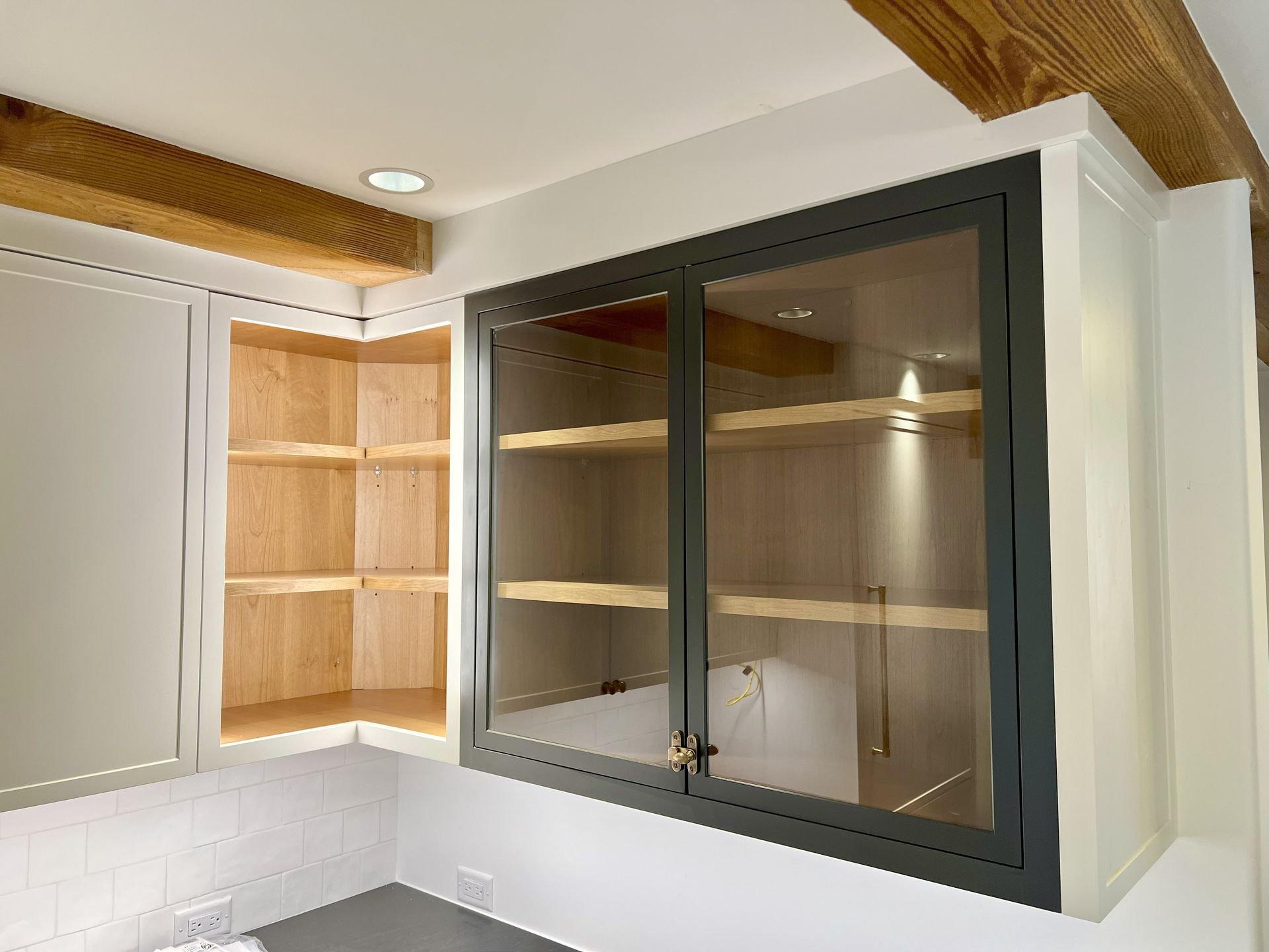 Kitchen cabinets with a glass-door cabinet and open corner cabinet; white, gray, and wood tones.