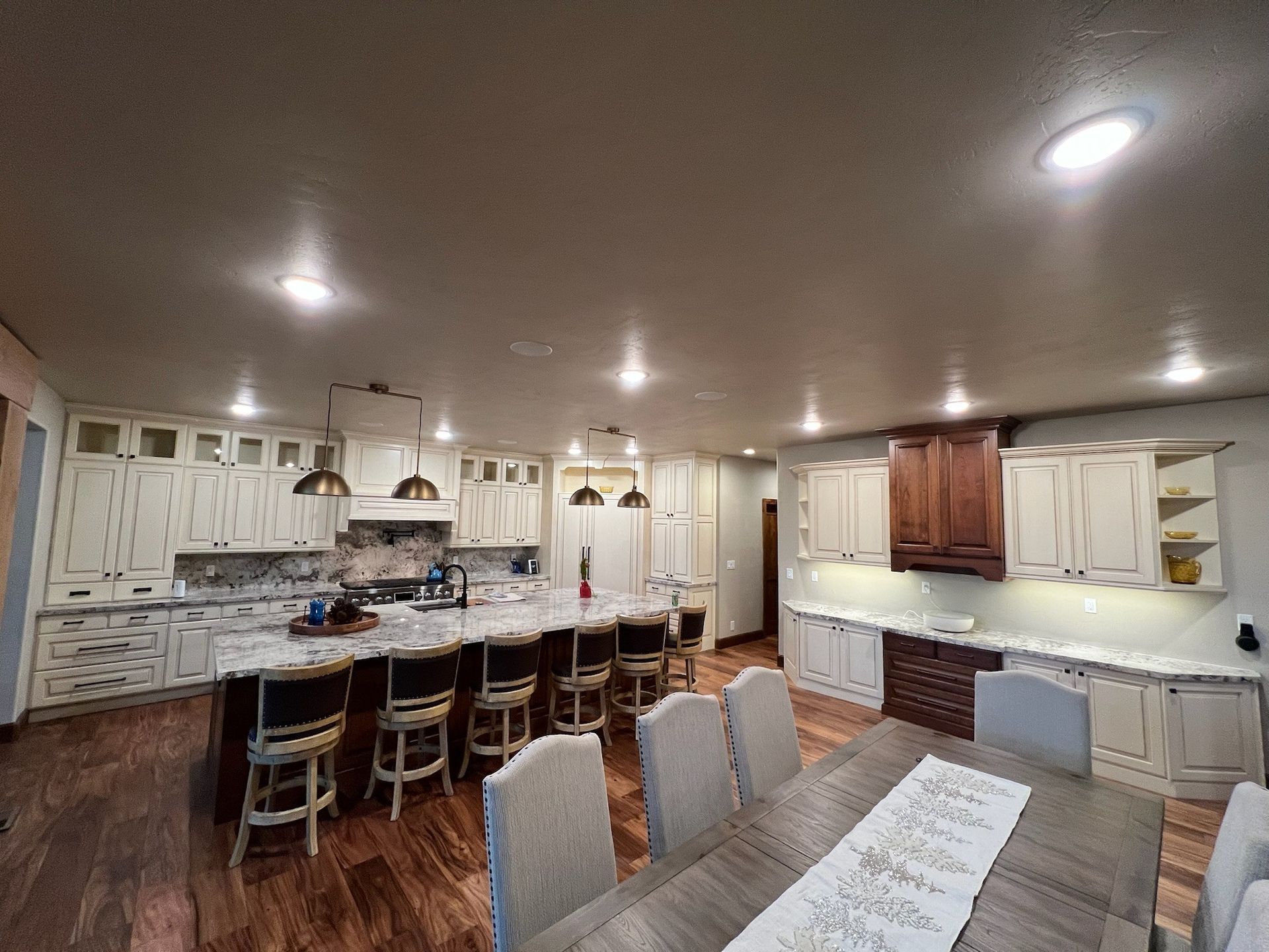 Spacious kitchen with cream cabinets, dark island and wood floor, centered by a dining table and chairs.