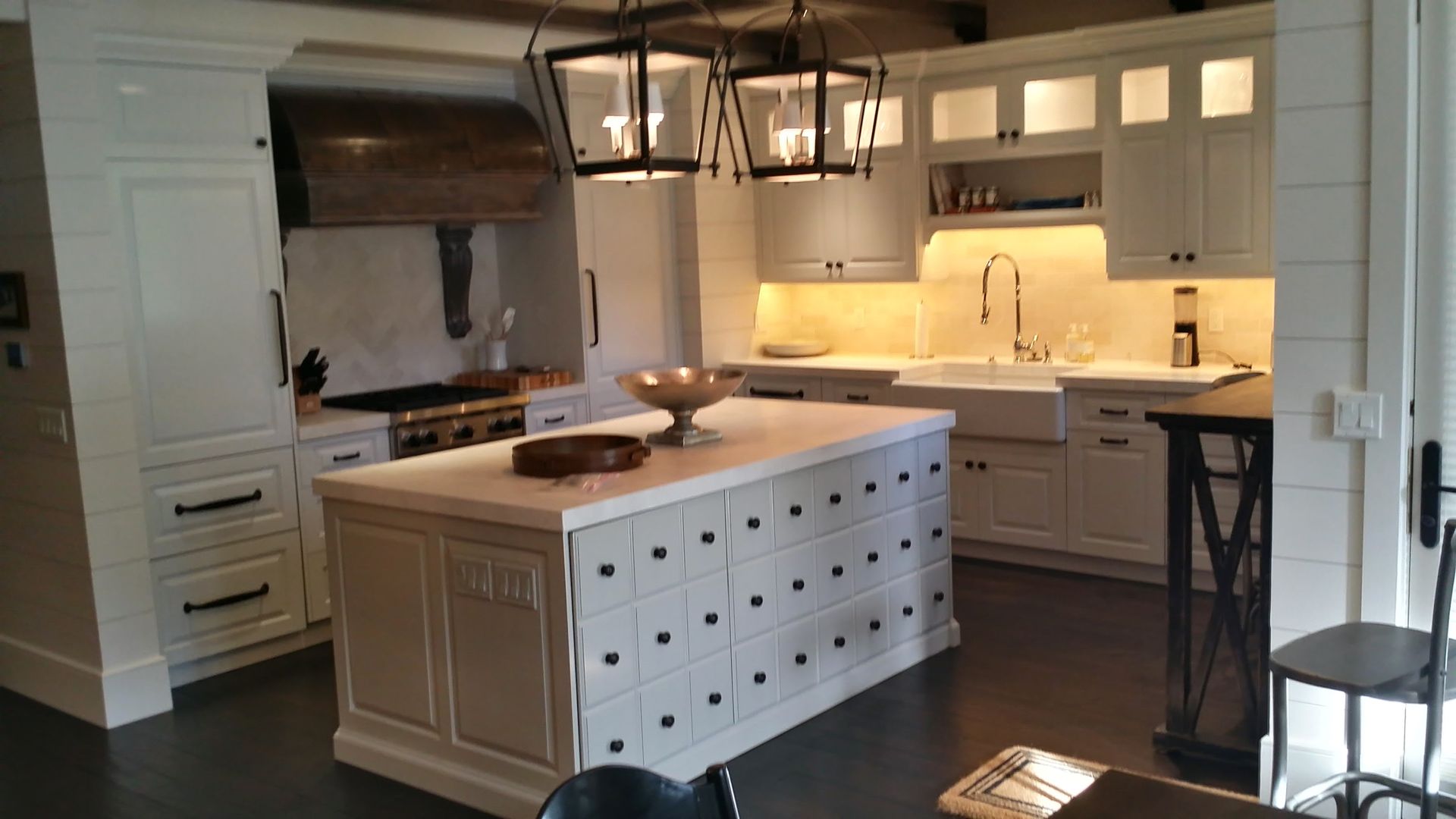 Elegant white kitchen with island, cabinets, wooden range hood, and lantern lighting.