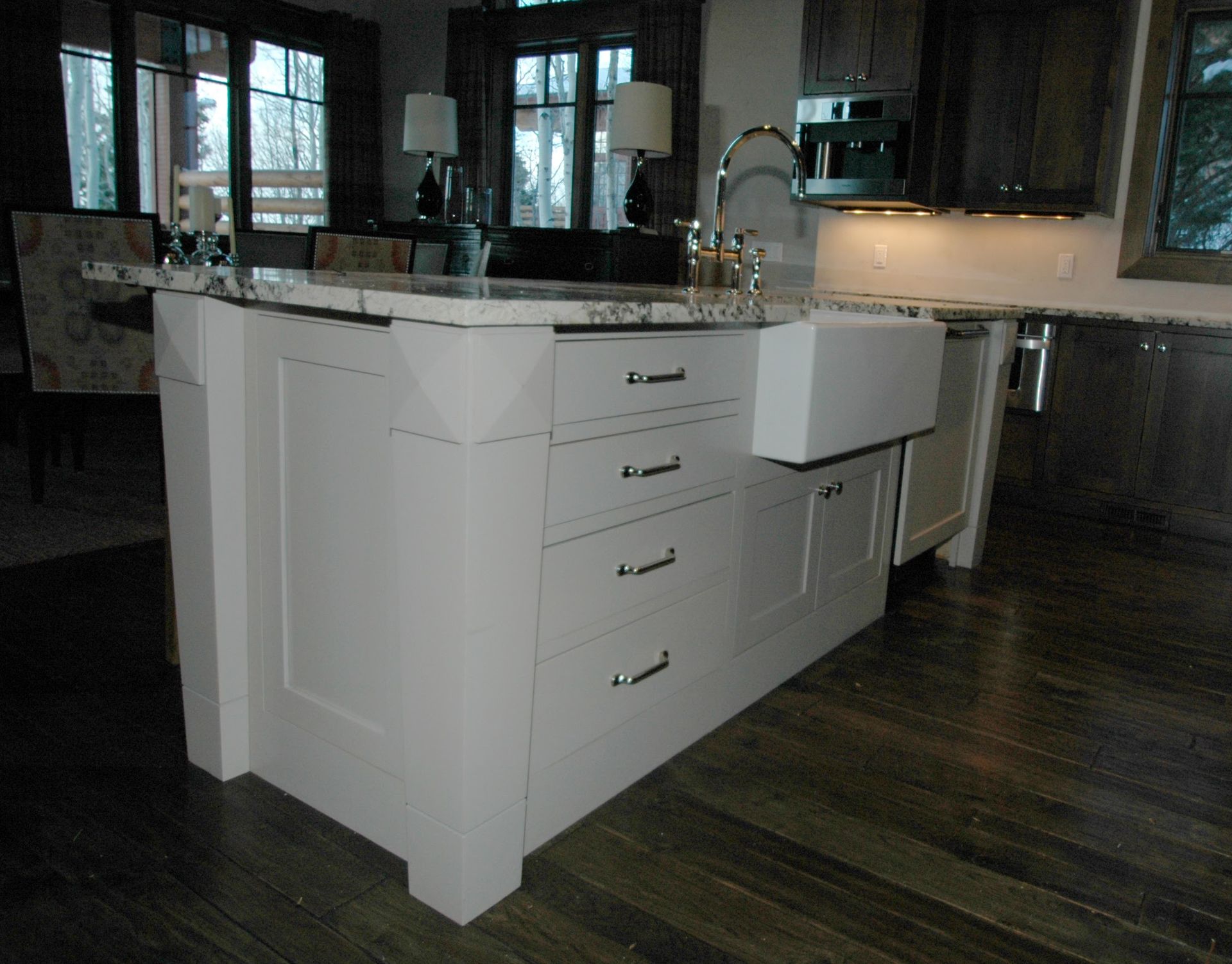 White kitchen island with drawers, farmhouse sink, and dark wood floor.
