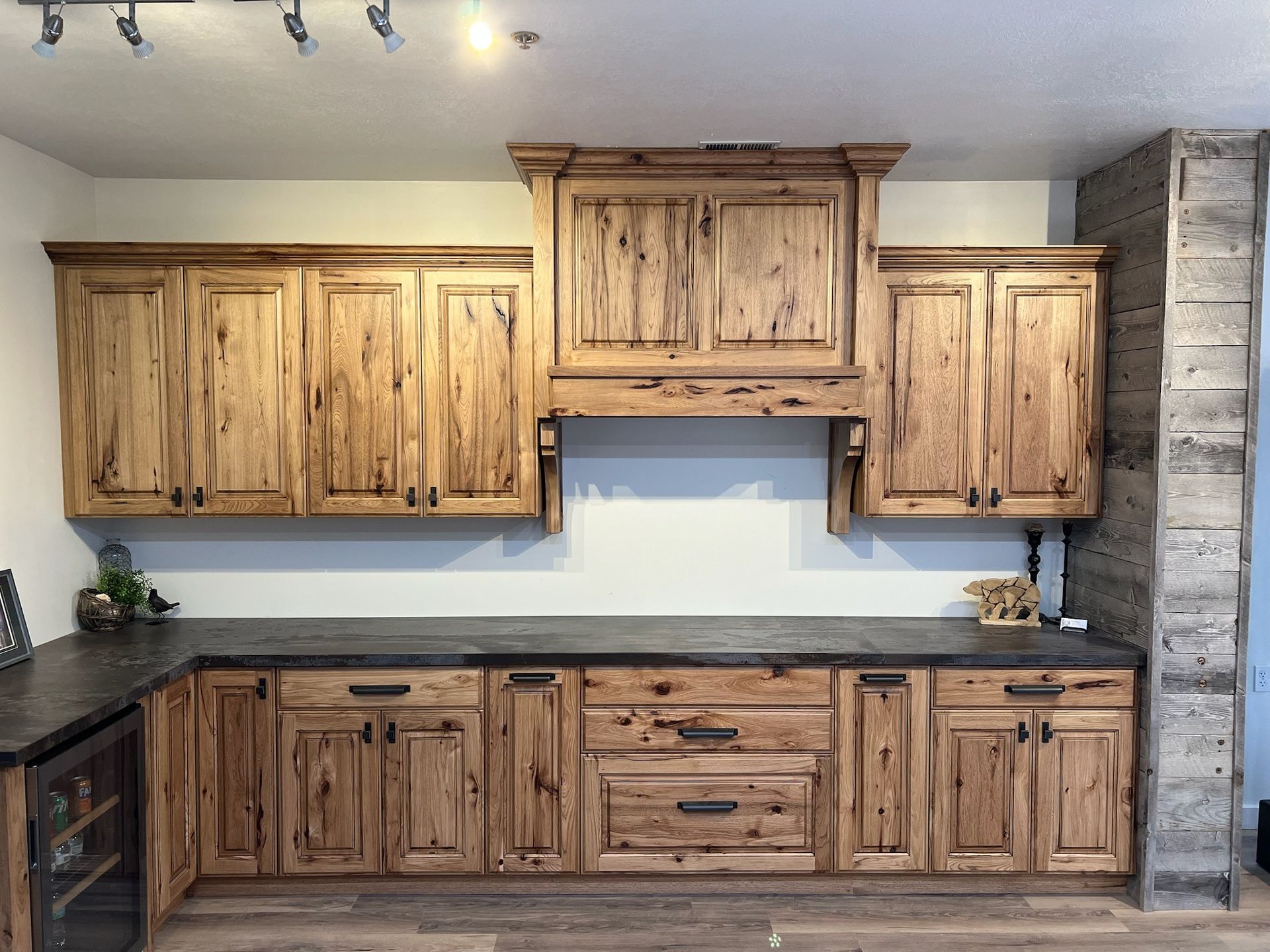 Rustic wood kitchen cabinets with dark countertops and wine fridge.