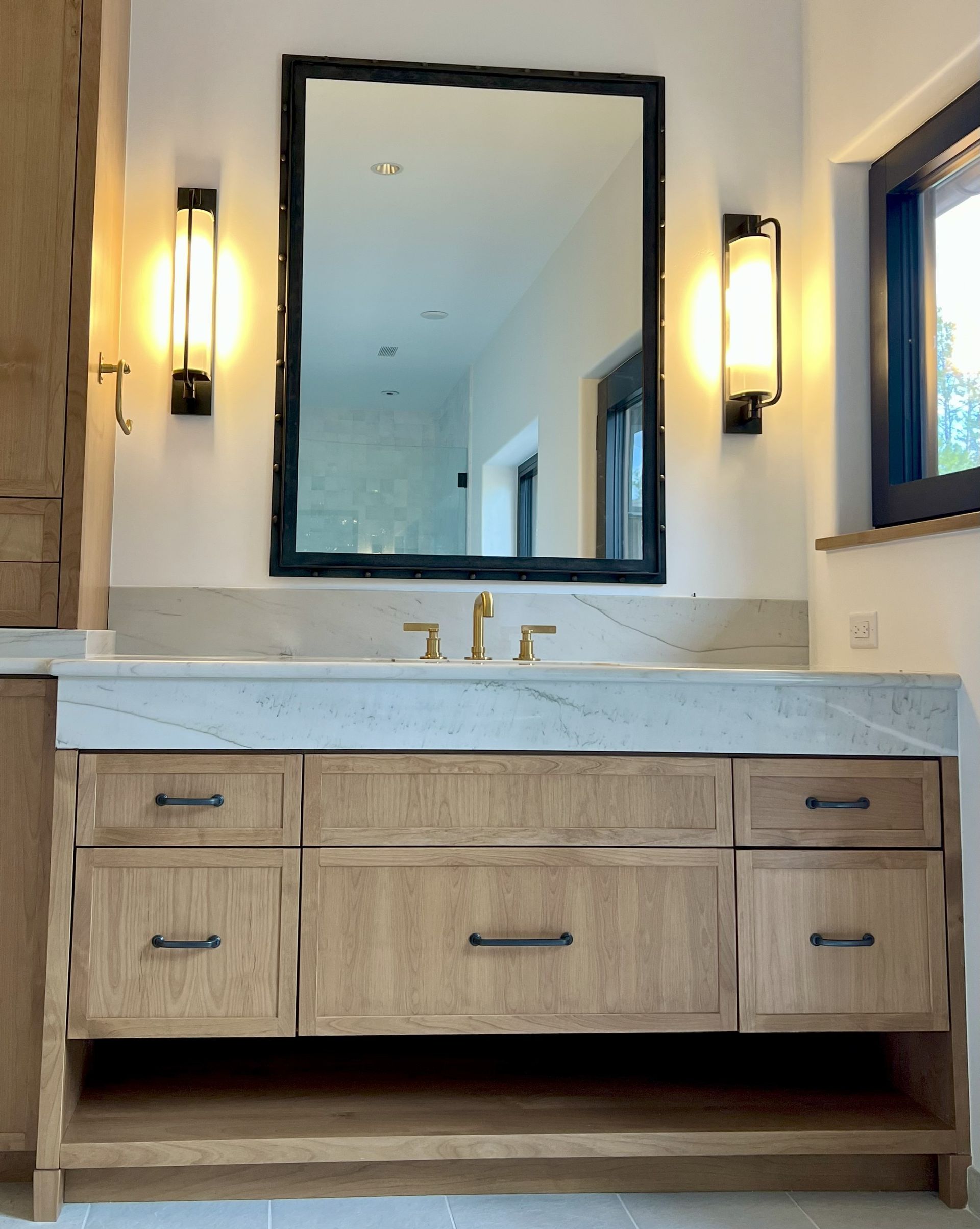 Wooden vanity with marble countertop, mirror, sconces, and gold faucet.