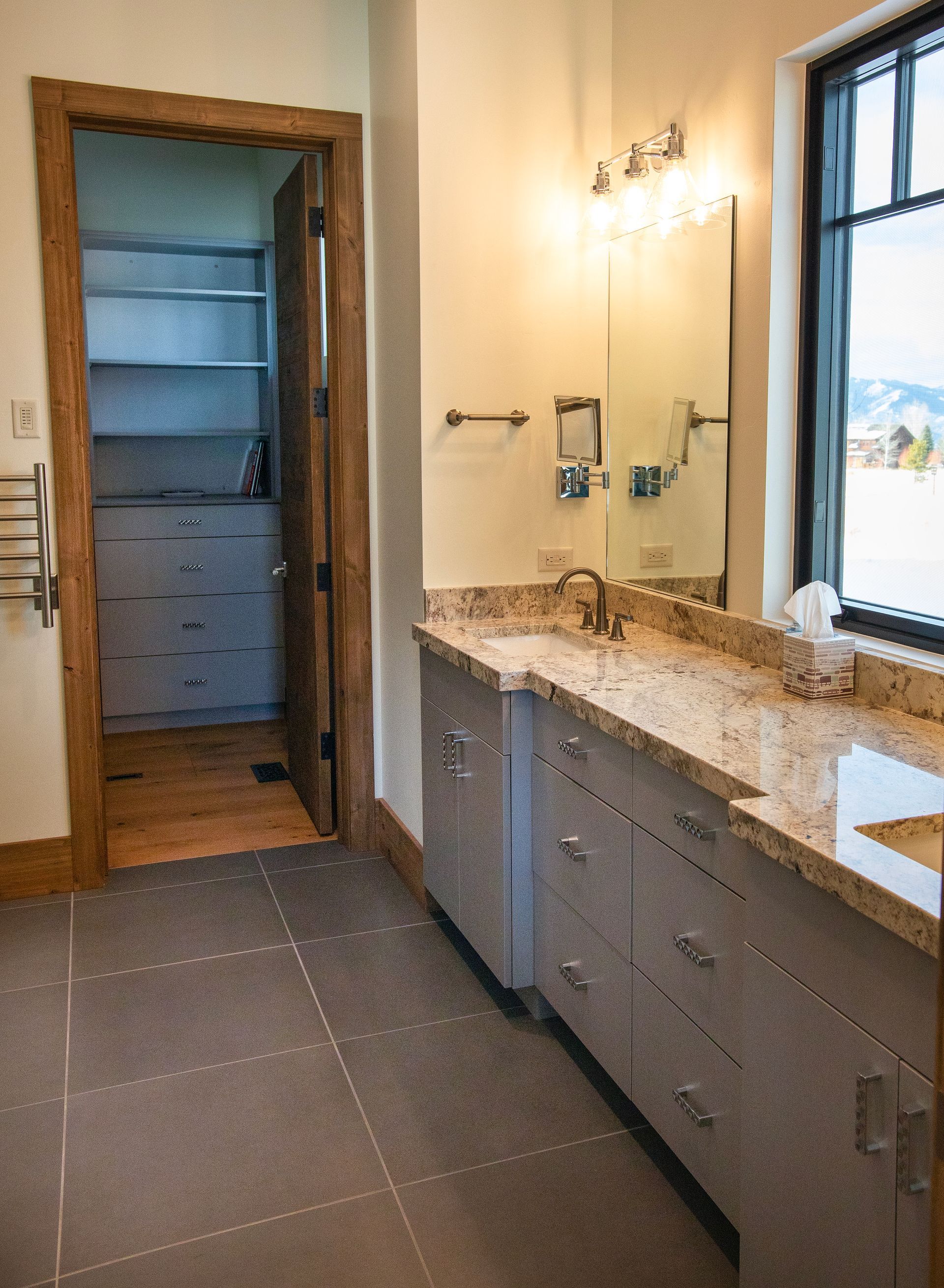 Bathroom with gray cabinets, granite countertop, closet, and window.