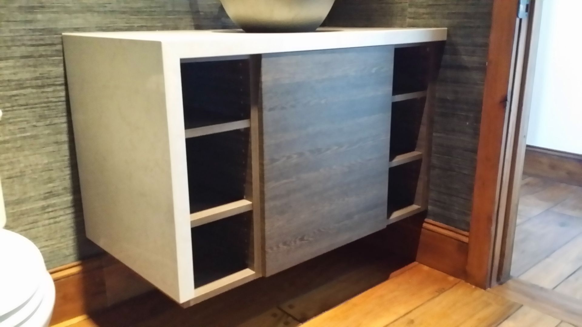 Floating gray cabinet with sliding door, open shelving, mounted on wall above wooden floor.