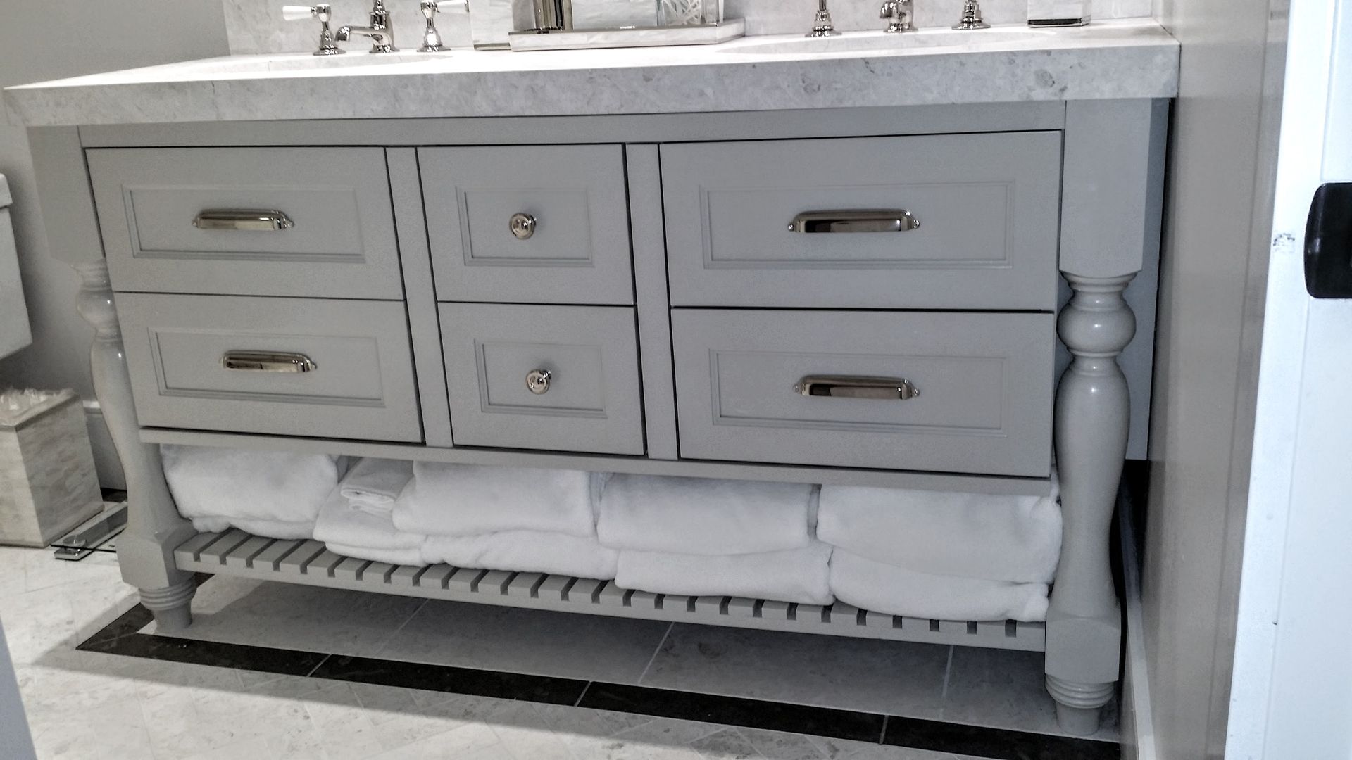 Gray bathroom vanity with drawers and towel shelf. White towels on the shelf.