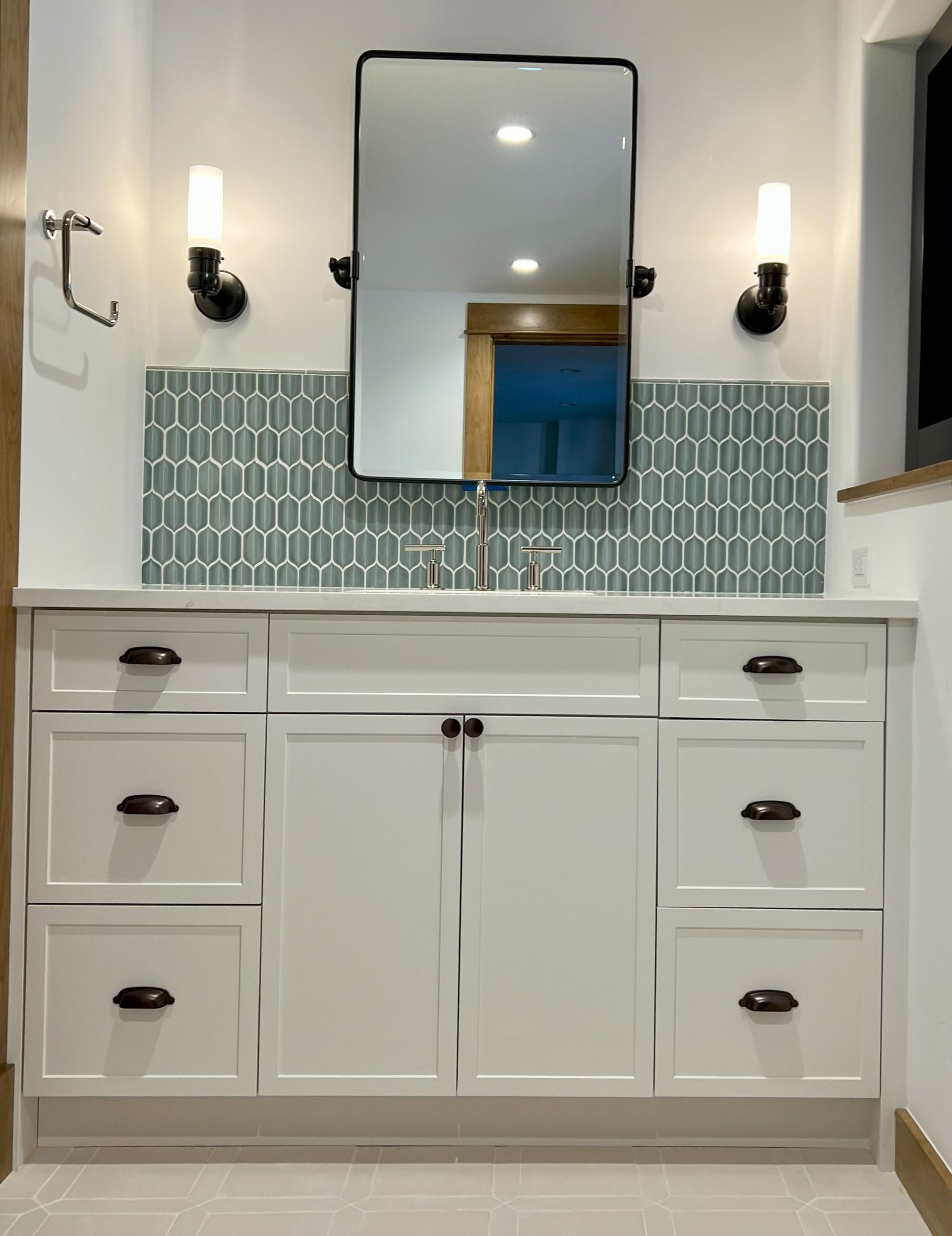 White bathroom vanity with a mirror, teal backsplash, and sconces.