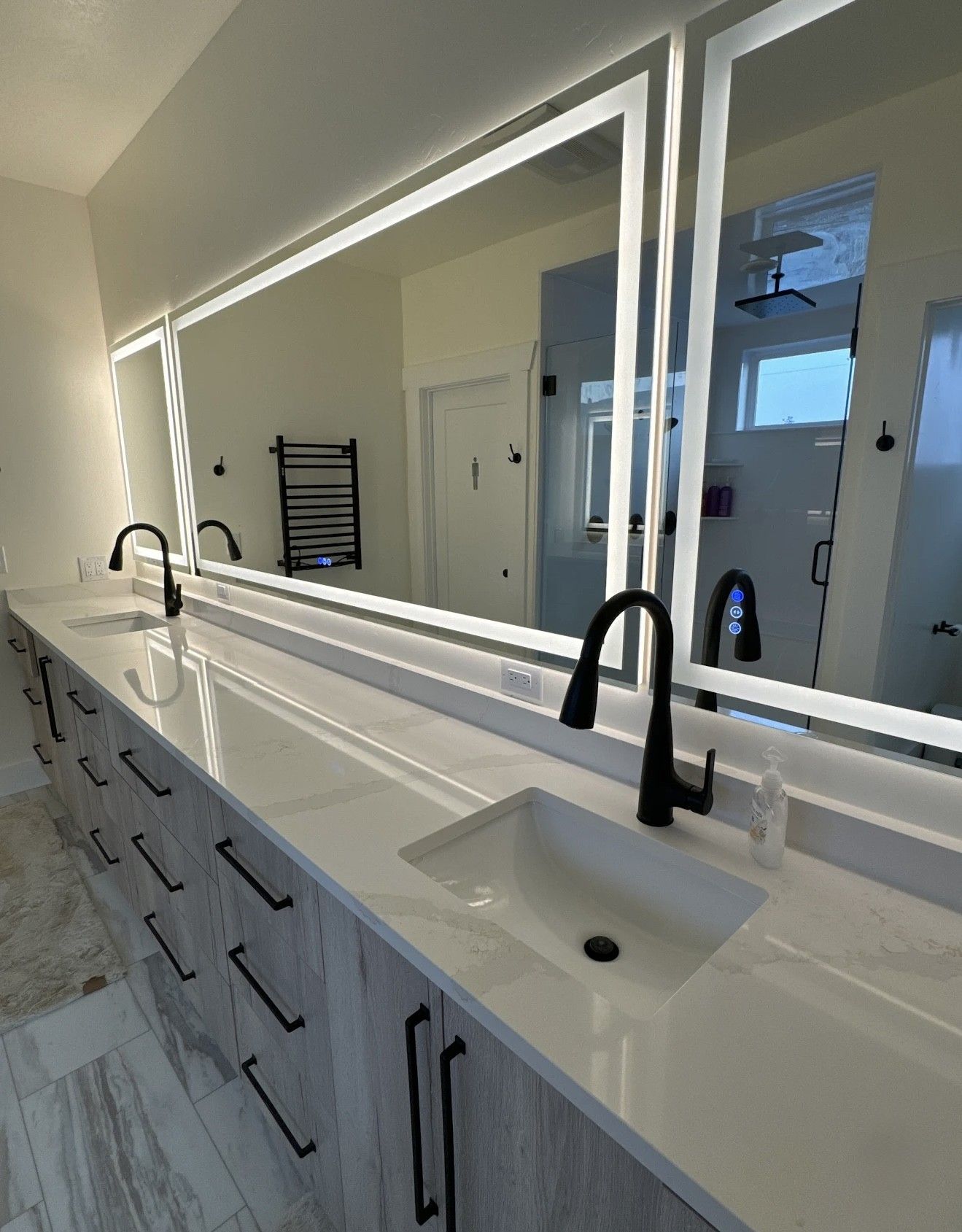 Bathroom vanity with marble countertop, black faucets, and lighted mirrors.