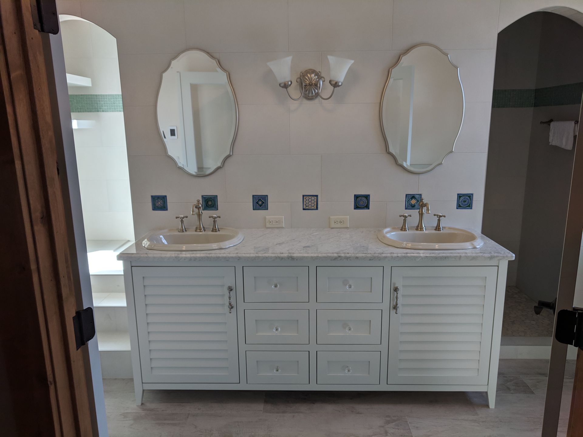 Bathroom with a white vanity, two oval mirrors, and blue tile accents.