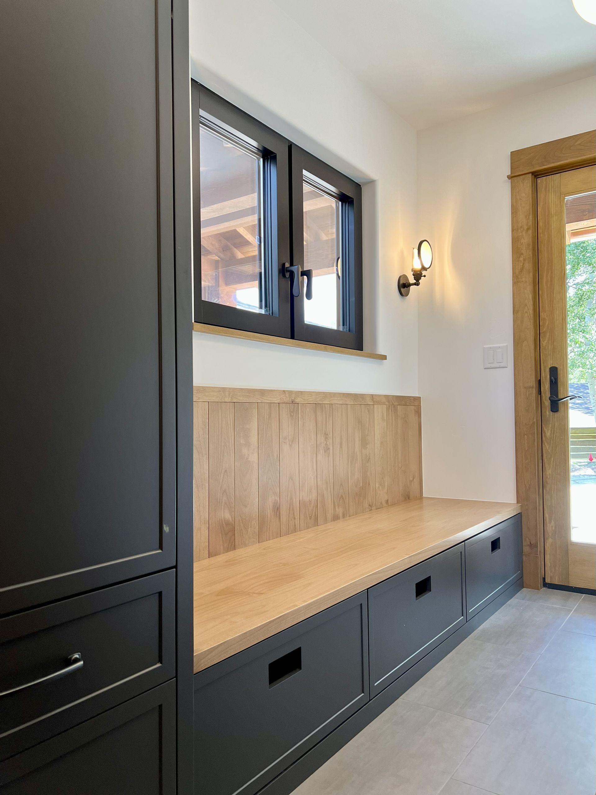 Built-in entryway bench with storage drawers, black cabinets, light wood accents, and a window.
