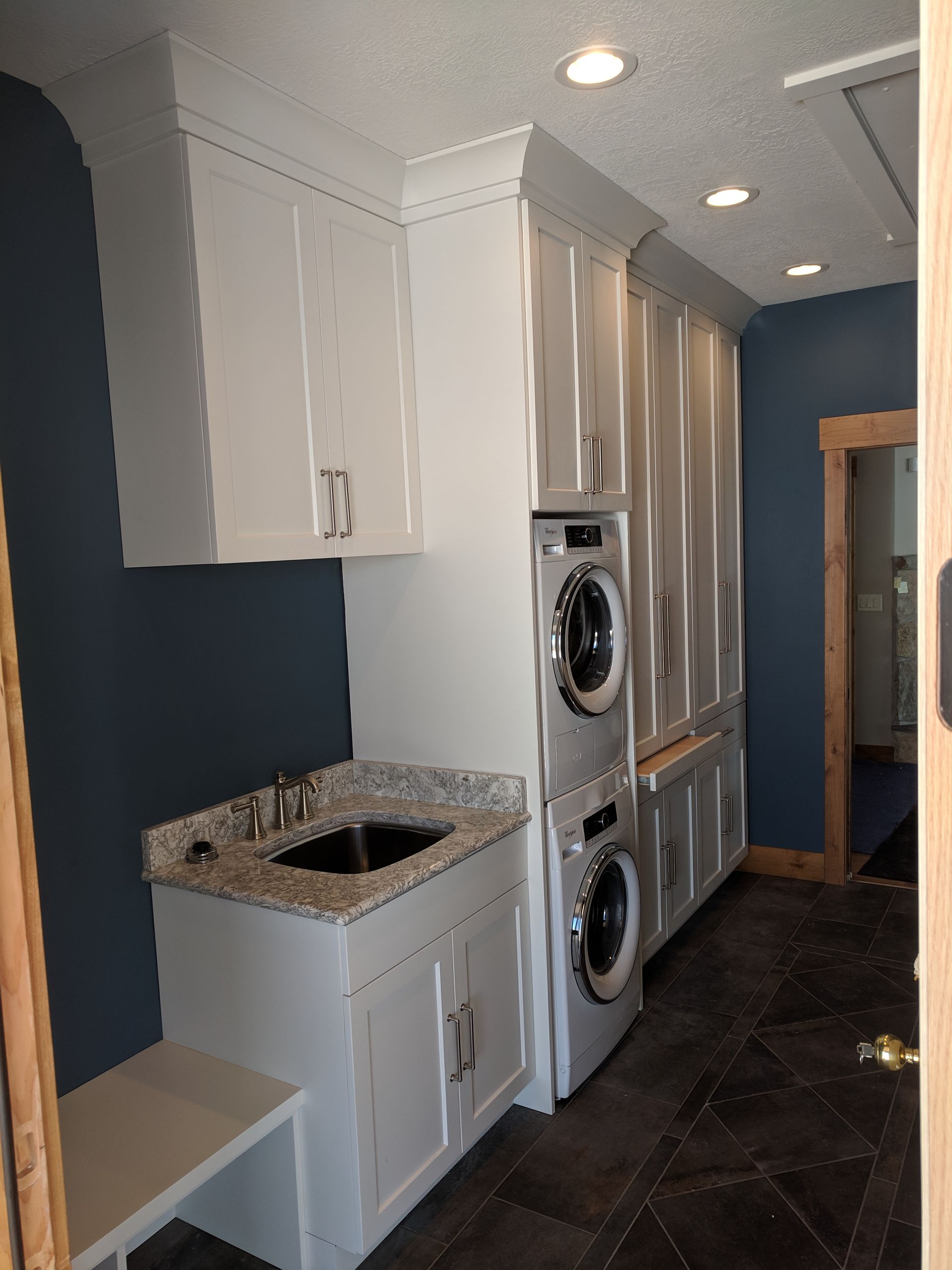 Laundry room with white cabinets, blue walls, stacked washer/dryer, sink, and a granite countertop.
