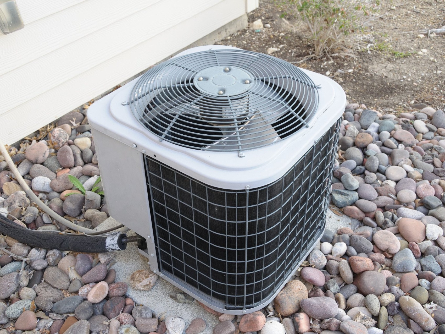 An air conditioner is sitting on a pile of rocks next to a house.