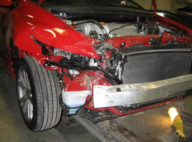 Red car severely damaged in front-end collision, showing crumpled metal, broken parts.