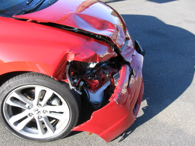 Red car with severe front-end damage, crumpled hood, and broken headlight.