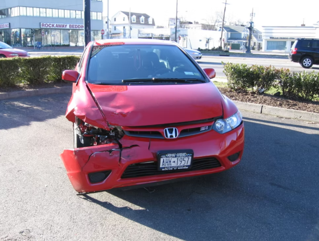 Red Honda Civic car heavily damaged on its front left side, on a sunny street.