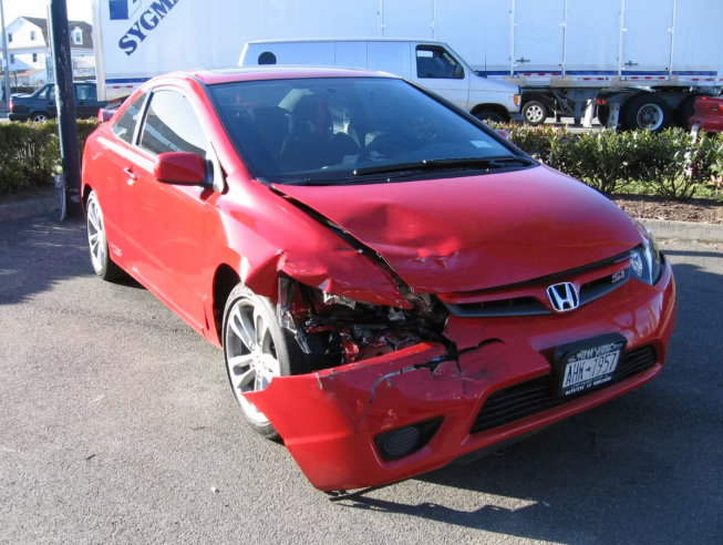 Red Honda Civic with significant front-end damage; accident scene; parked on pavement.