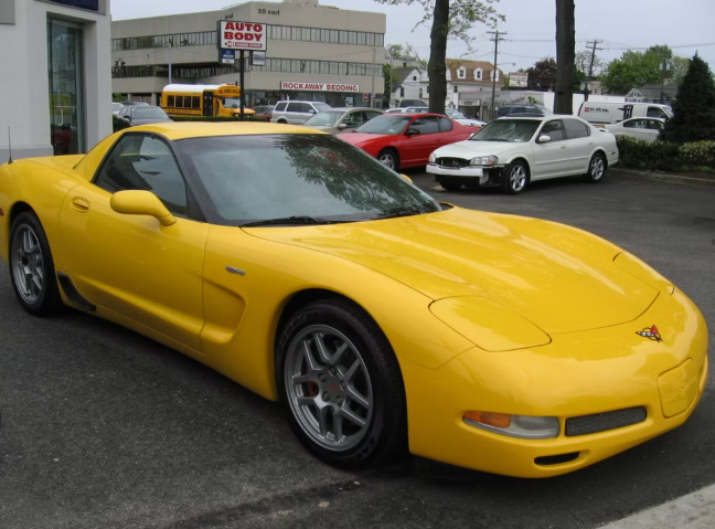 Yellow Corvette sports car parked in front of an auto repair shop on a cloudy day.