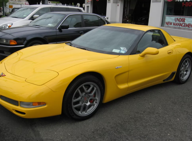 Yellow Chevrolet Corvette parked on a street. Other cars and building in the background.