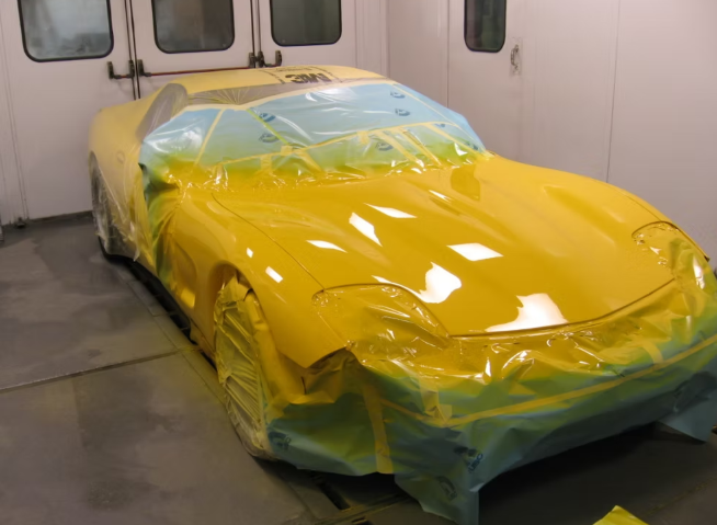 Yellow car masked for painting inside a paint booth.