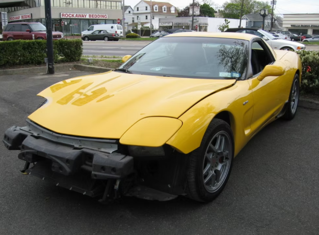 Yellow Corvette with front bumper damage, parked on a street.
